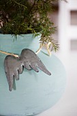 Metal angel's wings hung on turquoise plant pot