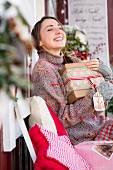 Young woman holding present and smiling on decorated veranda