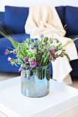 Glass vase of wild flowers on white side table in front of dark blue couch