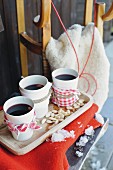 White beakers of mulled wine wrapped in fabric on wooden tray with wooden sledge in background
