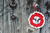 Picture of cow with round, crocheted frame on weathered board wall