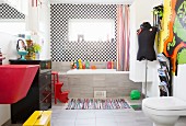 Red sink, black chest of drawers and fitted bathtub in bathroom with chequered wall tiles