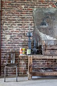Old workbench and metal chair below patinated mirror on brick wall