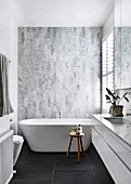 Designerbad mit freistehender Badewanne vor Marmorfliesen und schwarzen Bodenfliesen