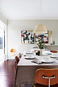 Classic wooden chairs around a laid table in a bright living room with a pendant lamp and modern art paintings