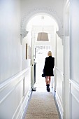 Hallway with white wood paneling and stucco arch, woman dressed in black in the background