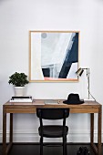 Minimalistischer Edelholz-Schreibtisch und schwarzer Bistrostuhl vor modernem Bild