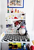 Baby-changing cabinet with black and white polka-dot mat next to shelves of toiletries and toys