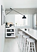 White kitchen counter, bar stools and black cantilever lamp on wall