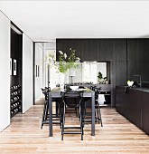 Counter table with black bar stools in an elegant, custom-made kitchen with black wooden fronts