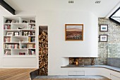 Open fire in modern fireplace with integrated fireplace bench and firewood stacked in vertical niche next to white fitted shelves