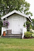 White wooden summerhouse with small veranda and hanging baskets