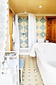 Free-standing white bathtub and shower in bathroom tiled in blue and beige