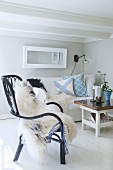 Sheepskin on black cane chair in front of scatter cushions arranged on sofa