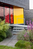 Metal steps and ramp leading into modern house with red glass terrace doors and yellow wall panel