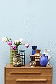 Retro ceramic vases on top of chest of drawers against wall painted pale blue
