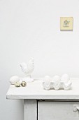 White eggs in egg box, quail eggs and cockerel ornament on top of cabinet