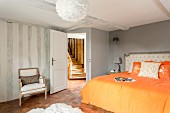 Double bed with orange bed linen in renovated bedroom with view of rustic wooden staircase