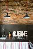Schwarze Beton-Küchenarbeitsplatte und Spritzschutz vor rustikaler Ziegelwand
