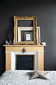 Gilt frames leaning against black wall on mantelpiece in bedroom