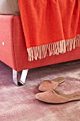 A red box spring bed with chrome plated feet and a red throw (detail)
