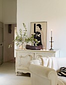 Olive branches, wooden bowl, candlestick, tealights and picture of woman on top of white vintage cabinet