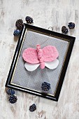 Hand-made felt butterfly in vintage picture frame surrounded by pine cones