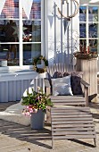 Lounger with cushions next to wintry flower arrangement on wooden terrace