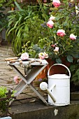 Vintage Gartenscheren auf Holzhocker neben Rosenblüten und weisser Gießkanne