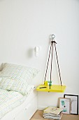 DIY shelf made from climbing ropes hung on wall as bedside table
