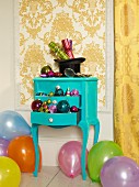Christmas decorations on top of and in drawers of turquoise console table amongst balloons on floor