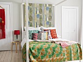 Four-poster bed with white-painted wooden frame, colourful patterned bedspread and retro-style scatter cushions