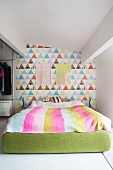 Colourful wallpaper on accent wall and green upholstered double bed frame in bright bedroom
