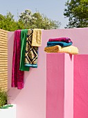 Towels stacked on pink wall in front of patterned towels draped over pink limewashed garden wall