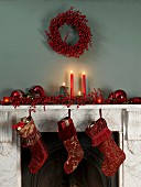 Mantelpiece festively decorated with Christmas stockings, lit candles and red decorations