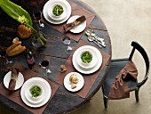Place settings with small bowls of salad on brown place mats on round wooden table