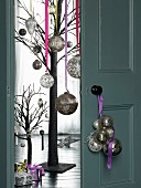 Christmas baubles hung from door knob, half-open double doors with view of stylised tree decorated with silver baubles and gifts on floor