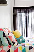 Colorful, geometrically patterned bed linen with matching pillows in front of windows with black curtains