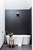 Freestanding bathtub with stand mixer in front of black wall covering in a simple bathroom