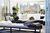 Tagesliege vor gemütlicher Couch mit weissen Polstern in Wintergartenanbau mit Zimmerpflanzen