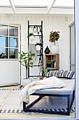 Couch, potted plants hung from black ladder frame in conservatory extension with Scandinavian ambiance