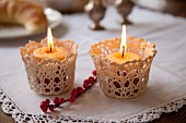 Romantic arrangement of two lit candles in crocheted holders on white tablecloth