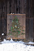 DIY bird-feeding station shaped like Christmas tree made from green cord on rustic wooden panel
