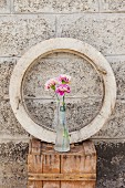 Three carnations in glass bottle in front of round window frame on wooden crate