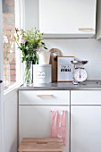 Kitchen scales, glass vase of flowers and bread bin on white kitchen cabinets