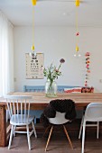 Various chairs around solid wooden dining table, flowers in large glass jar, eye chair on wall and crocheted garland