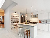 Free-standing counter below copper pendant lamps in open-plan modern kitchen with white cupboards