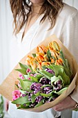 Woman holding bouquet of tulips of various colours wrapped in paper
