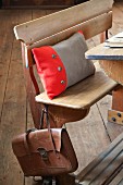 Scatter cushion with two-tone boiled-wool cover on vintage school bench with old-fashioned leather satchel hanging from backrest