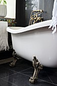 Free-standing, vintage bathtub with brass claw feet on black tiled floor